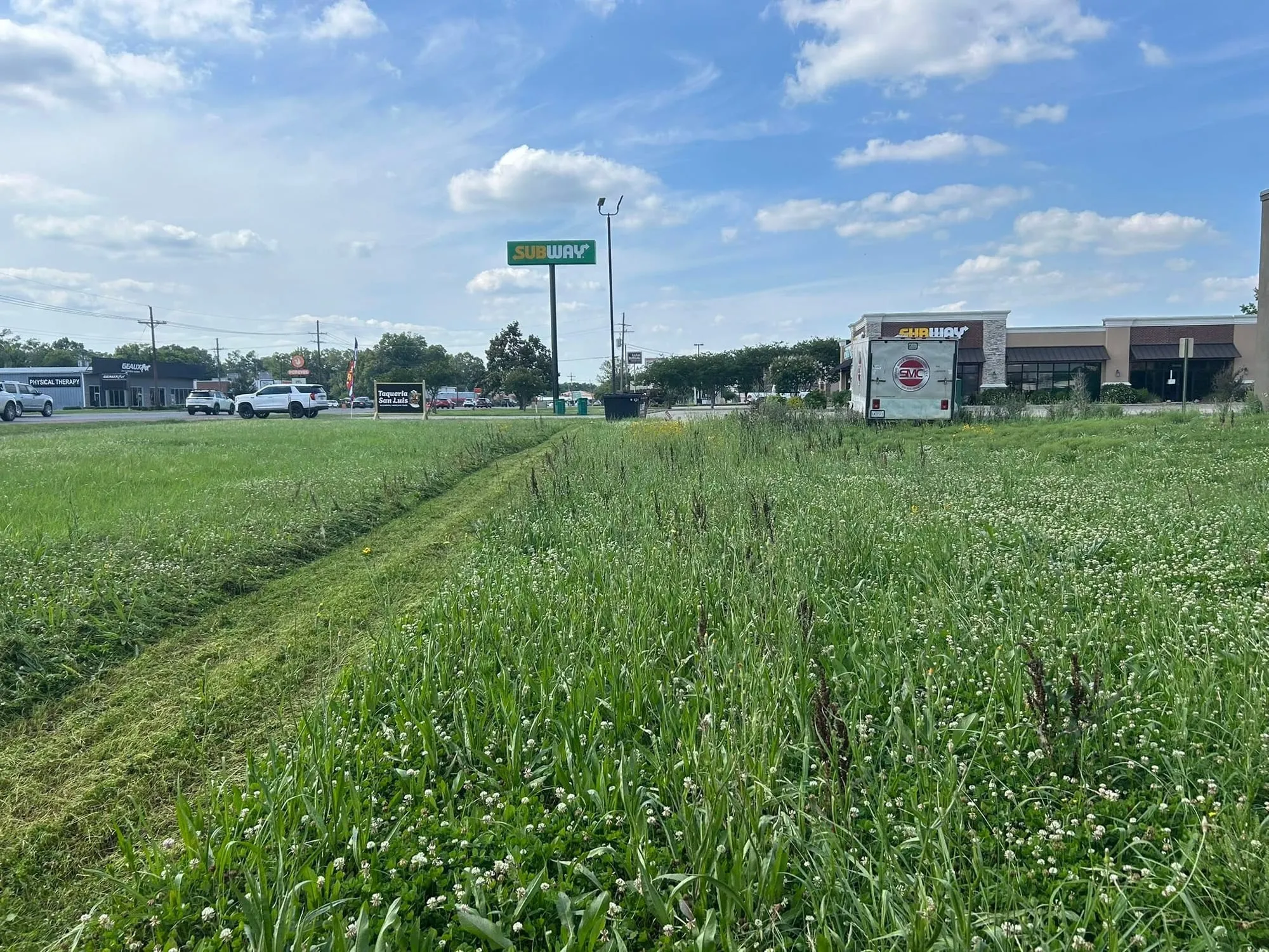 Overgrown commercial lot being mowed down, half cut and half tall grass