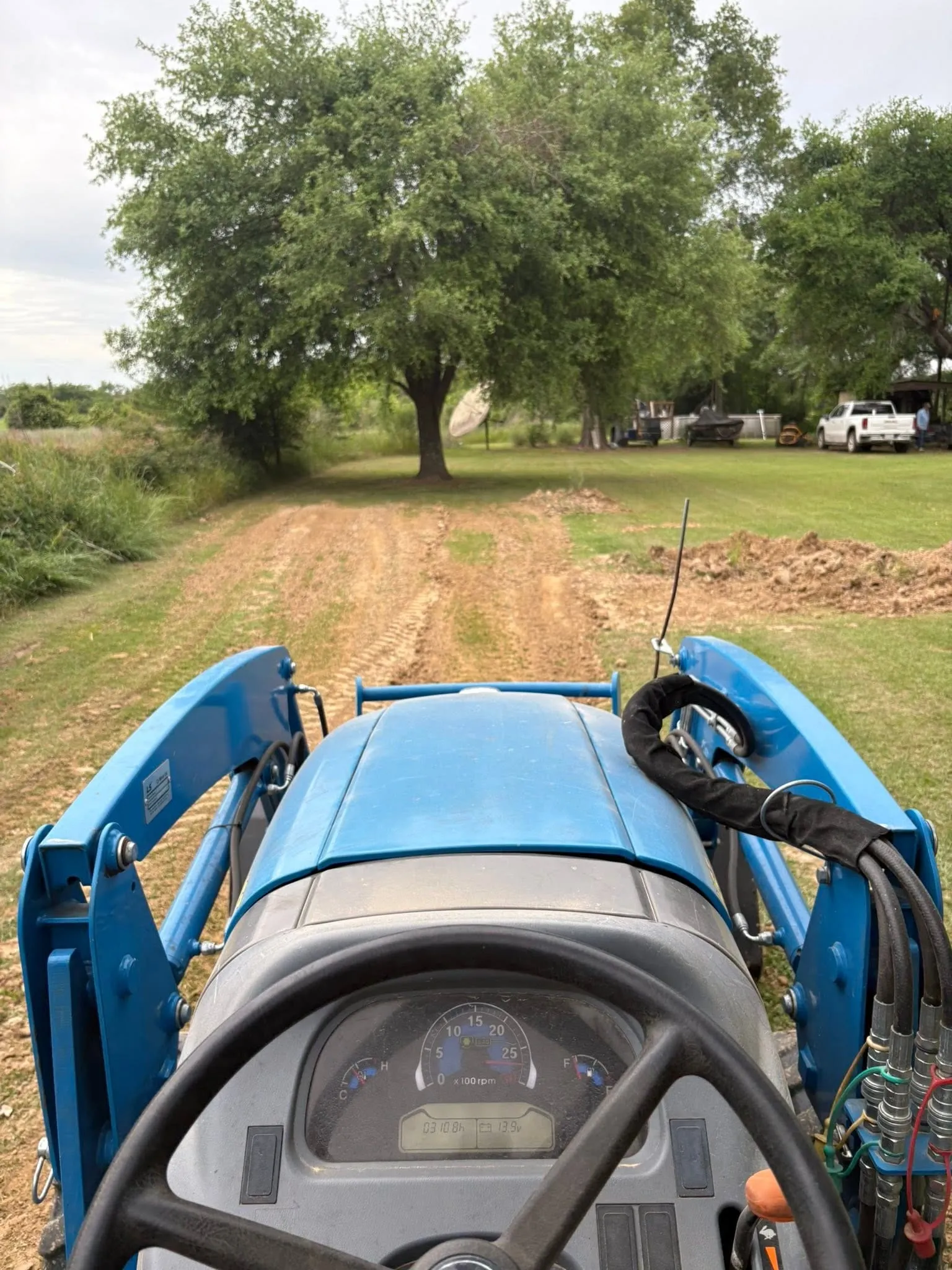 Tractor grading a dirt driveway smooth between grassy shoulders