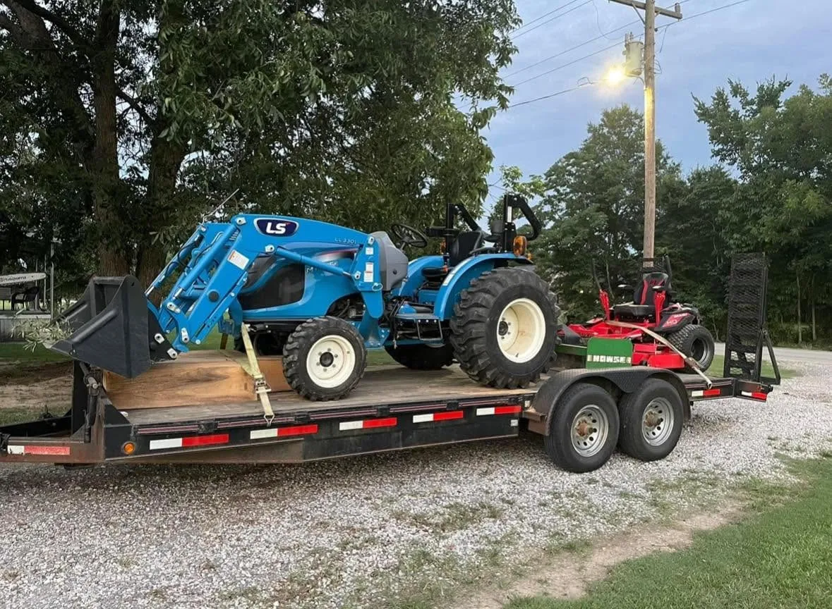 Tractor and zero-turn mower loaded together on a trailer at dusk