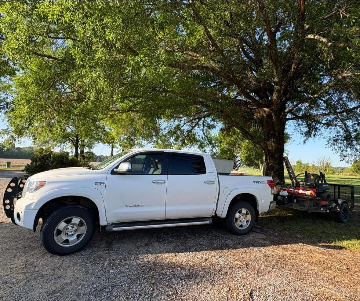 Bird & Bear truck and equipment trailer parked under a pecan tree before a job